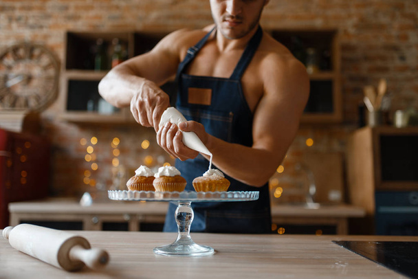 Γυμνός άντρας με ποδιά μαγειρεύει επιδόρπιο στην κουζίνα. Γυμνός άνδρας που ετοιμάζει πρωινό στο σπίτι, γυμνή προετοιμασία φαγητού - Φωτογραφία, εικόνα