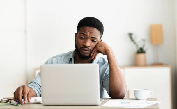 Verveelde zwarte werknemer op zoek naar laptop scherm, kan zich niet concentreren - Foto, afbeelding