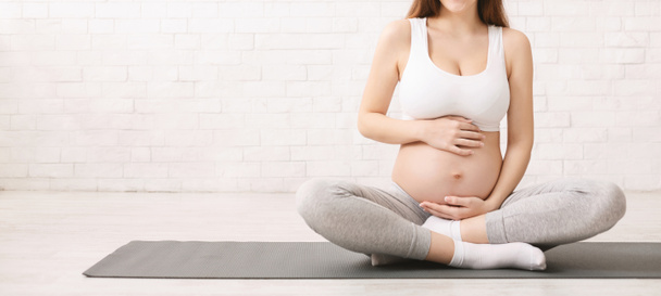Femme enceinte en tenue de sport assise sur un tapis de fitness
 - Photo, image