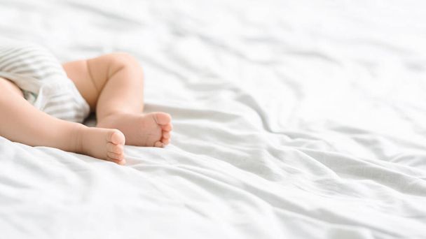 Fechar os pés de bebê infantil deitado na cama em bodysuit
 - Foto, Imagem