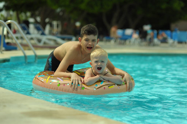 Crianças na piscina, felicidade e alegria. Dois irmãos se divertindo nadando anel
 - Foto, Imagem