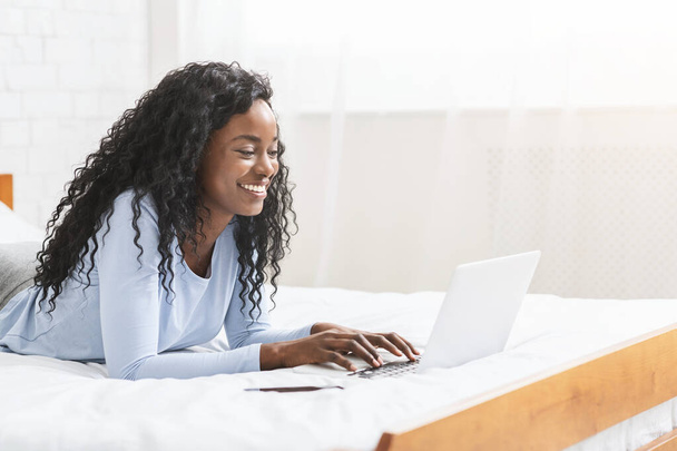 Cheerful young girl typing on laptop in bedroom - Photo, Image