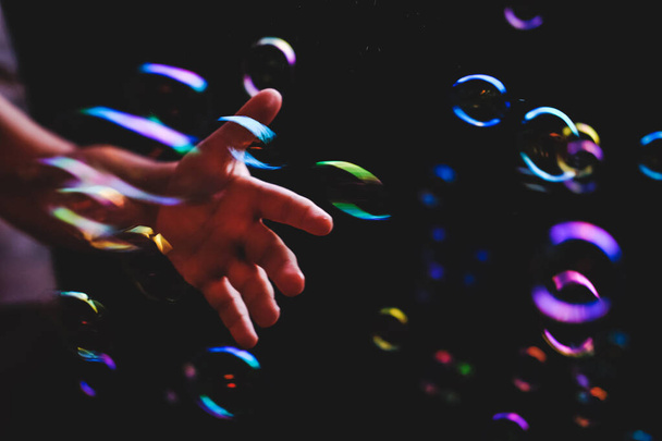 Mano tratando de atrapar burbujas de colores sobre fondo oscuro
 - Foto, Imagen