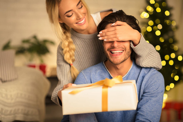 Happy woman surprising husband with Christmas gift - Fotoğraf, Görsel