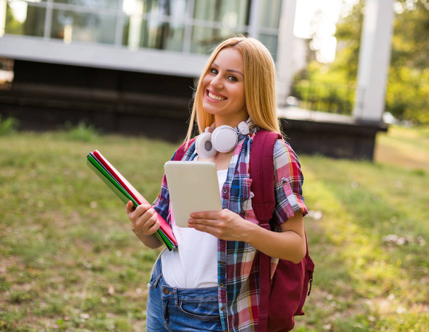 Female student with headphones using digital tablet outdoor. - Foto, afbeelding