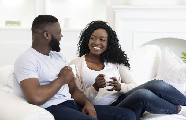 Happy black couple relaxing on couch and drinking coffee - Photo, Image