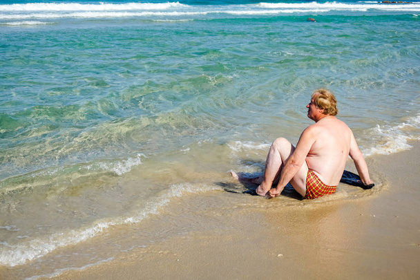 Um homem idoso com nadadeiras descansando na praia
 - Foto, Imagem