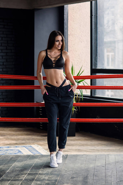 Sexy fitness girl in sportswear stands leaned on ropes of boxing ring. - Photo, image