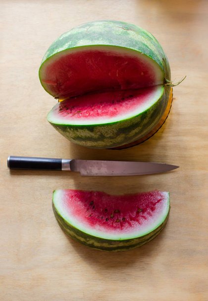 Zusammensetzung aus Wassermelone und Messer. Wassermelone in Scheiben geschnitten auf einem Tisch mit einem Messer in der Mitte. - Foto, Bild
