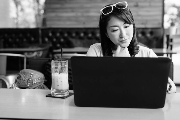 Madura mujer asiática utilizando ordenador portátil en la cafetería
 - Foto, imagen