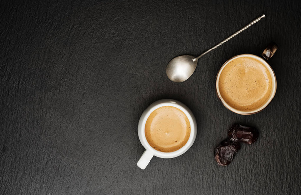 Twee kopjes espresso, zwart-wit, op een donkere stenen achtergrond. Bijna dateert fruit. Bovenaanzicht. Ruimte voor tekst. Een vergadering. - Foto, afbeelding
