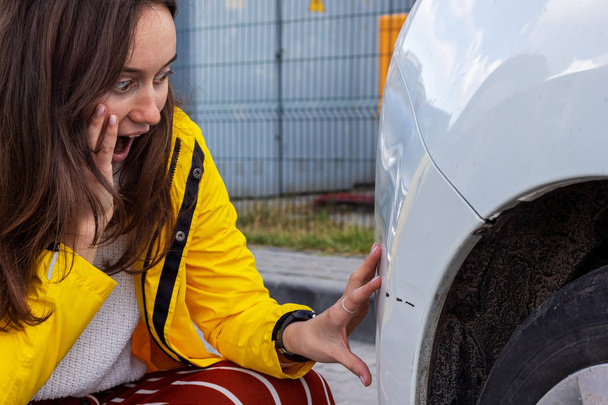 Bang, hulpeloos en verrast vrouw kijkt naar haar beschadigde gekrast auto. - Foto, afbeelding
