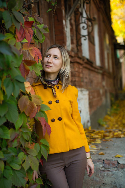 Egy sárga kabátos nő áll egy régi ház mellett az őszi hangulatban.. - Fotó, kép