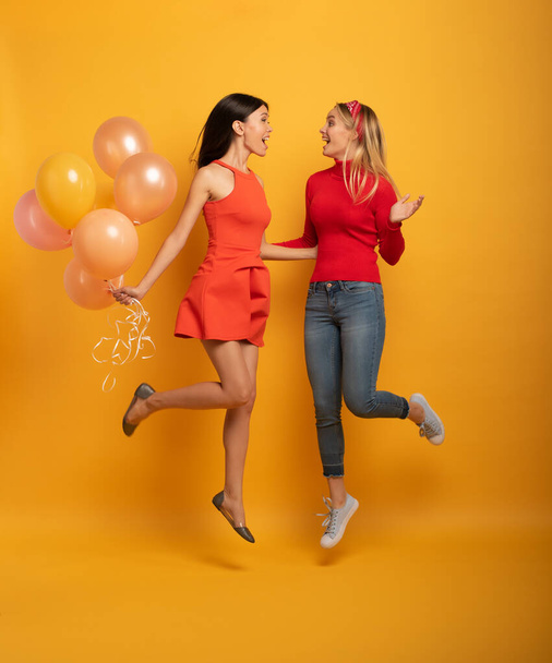 Girls ready for a party with balloons. Joyful an happiness expression. Yellow background - Photo, Image