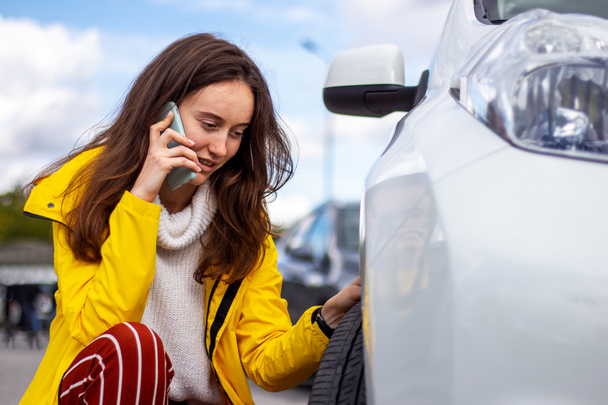 Una donna sconvolta che parla al telefono vicino a un'auto rotta. Pneumatico perforato. Sfida dell'evacuatore
. - Foto, immagini