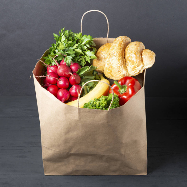 sacchetto di carta pieno di vari alimenti e verdure con frutta su sfondo di legno nero. concetto di imballaggi ecologici di materiali riciclabili
 - Foto, immagini