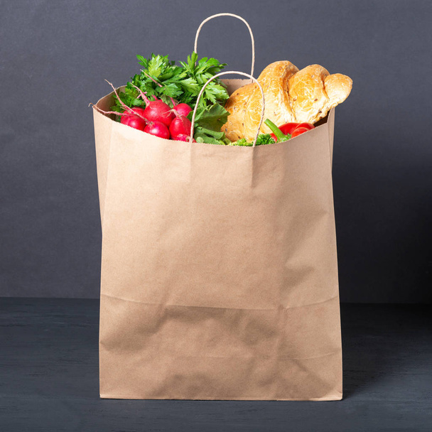 bolsa de papel llena de varios alimentos y verduras con frutas sobre fondo de madera negro. concepto de envases ecológicos de materiales reciclables
 - Foto, imagen