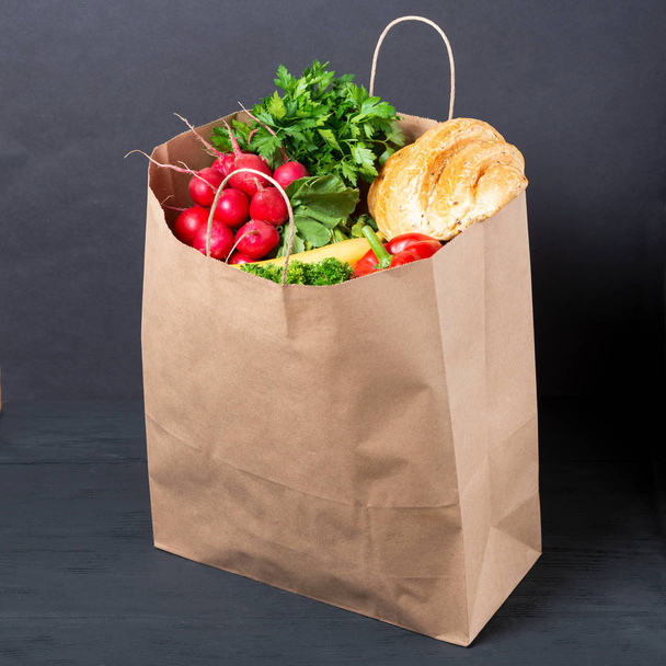 full paper bag of various foods and vegetables with fruits on black wooden background. concept of eco packages of recyclables - Photo, Image