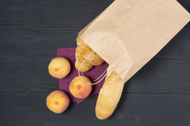 full paper bag of various foods and vegetables with fruits on black wooden background. concept of eco packages of recyclables - Фото, зображення