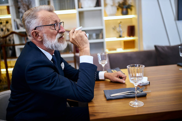 Senior man holding and smoke e-cigarette in restaurant . IQOS, modern technologies. - 写真・画像