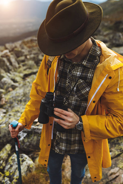 young guy in shirt, yellow coat, green hat has problems with binocular - Фото, изображение