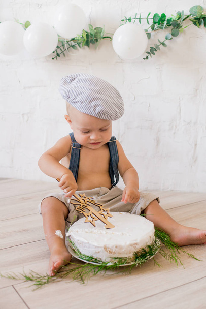 Cute little boy with a birthday cake on his first birthday with white balloons and vintage clothes - Photo, image