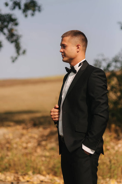 schöner Bräutigam trug eine Krawattenfliege. Hochzeitstag. Mann draußen. Junger Mann lächelt - Foto, Bild
