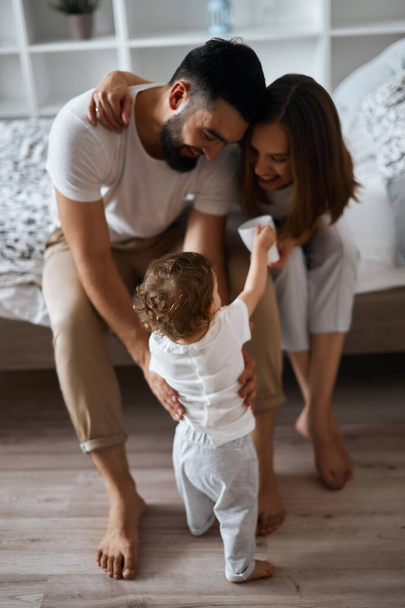 attractive cheerful parents teaching baby to walk - Photo, image