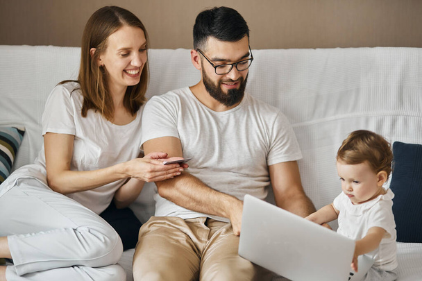 smiling parents holding credit card, while their child browsing the net - Valokuva, kuva