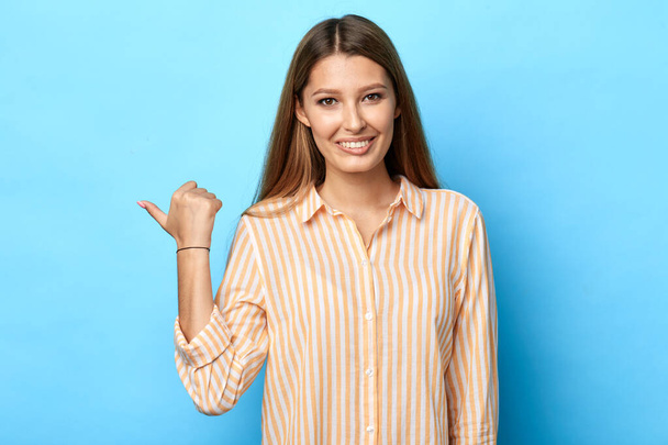 girl pointing with thumb aside looking at the camera over blue background - Фото, зображення