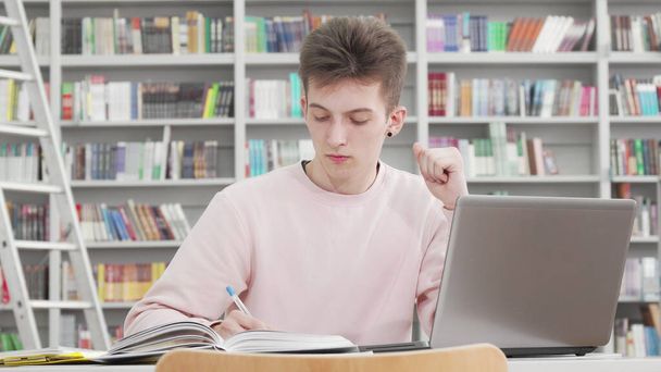 Молодий студент-чоловік працює на ноутбуці в бібліотеці коледжу
 - Фото, зображення