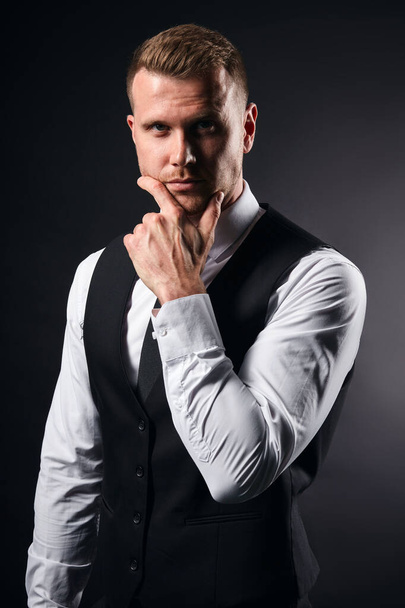 handsome serious man in elegant suit touching his chin with a palm - Фото, зображення