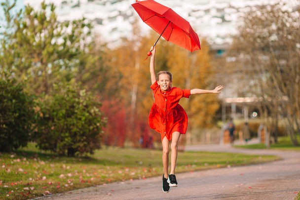 gelukkig kind meisje lacht onder rood paraplu - Foto, afbeelding