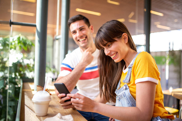 Close up portrait of boy friend and girl friend sitting at cafe and looking at cellphone together - Photo, Image