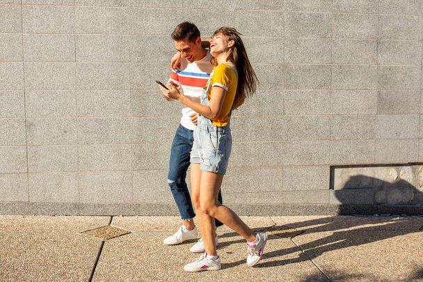 Täyspitkä puoli muotokuva poikaystävä ja tyttöystävä kävely ulkona matkapuhelin
 - Valokuva, kuva