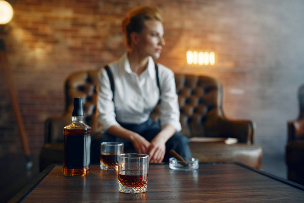 Woman in shirt and trousers sitting at the table with whiskey and cigar, retro fashion, gangster style. Vintage business lady - Fotografie, Obrázek