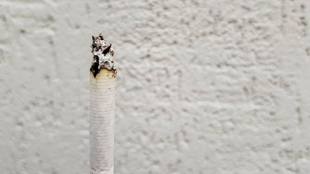 二次喫煙の概念。タバコのない日には、喫煙は社会にとって好ましくない。コピースペースの白い壁の背景に垂直タバコの喫煙。タバコのないテキスト. - 写真・画像