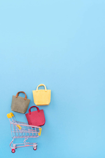 Abstract design element, annual sale, shopping season concept, mini yellow cart with colorful paper bag on pastel blue background, top view, flat lay - 写真・画像
