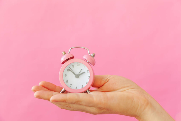 Diseño simple mujer mujer mano sosteniendo timbre doble campana reloj despertador aislado en rosa pastel colorido fondo de moda
 - Foto, Imagen