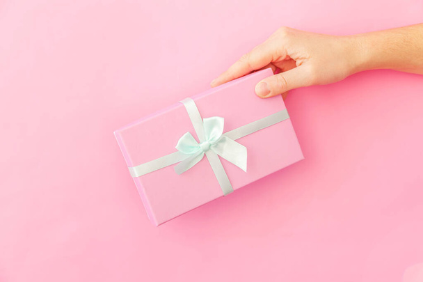 Simply design female woman hand holding pink gift box isolated on pink pastel colorful trendy background - Photo, Image