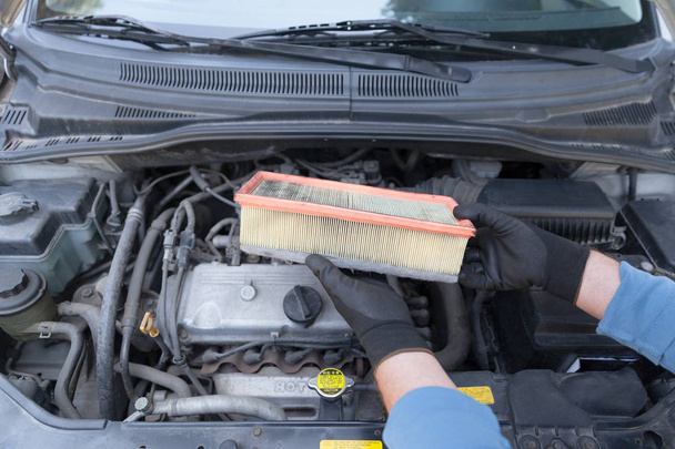 Otomobil tamircisi koruyucu iş eldivenleri giyer ve bir araba motoru üzerinde kullanılmış hava filtresi taşır. - Fotoğraf, Görsel
