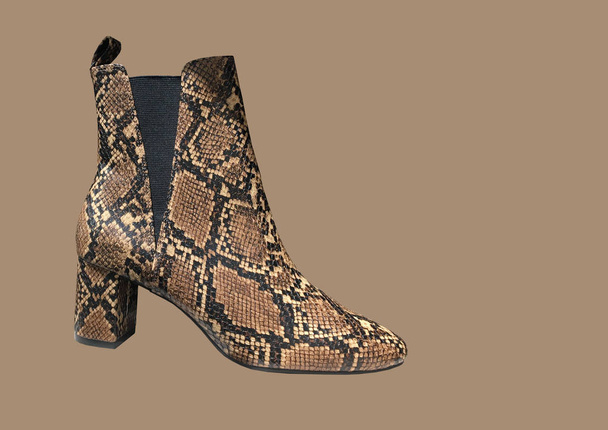 Women's Snakeskin Cowboy Boots isolated on brown background. Snake Cowboy Ankle Boots pattern. Close View Of Fashion Casual Female shoes. Brown snake Print Women Boots. Copy space - 写真・画像