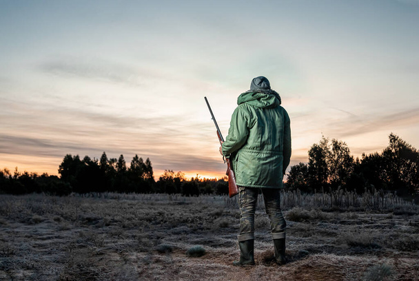 Hunter man in camouflage with a gun during the hunt in search of wild birds or game on a beautiful sunset. The concept of a hobby, killing. - Fotó, kép
