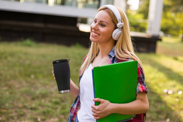Estudante feminina com fones de ouvido gosta de ouvir música e beber café ao ar livre
. - Foto, Imagem