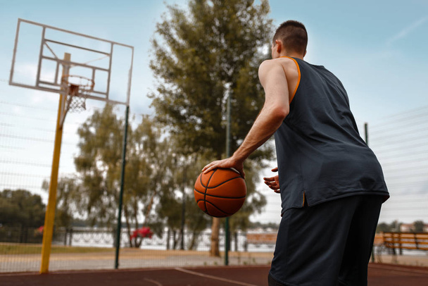 Jugador de baloncesto se prepara para hacer un lanzamiento en la cancha al aire libre. Atleta masculino en ropa deportiva sostiene la pelota en el entrenamiento de streetball
 - Foto, imagen
