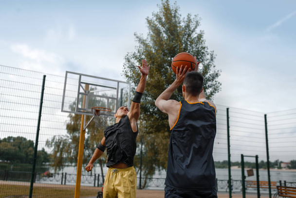 Two basketball players play the game on outdoor court. Male athletes in sportswear on streetball training in park - Photo, image