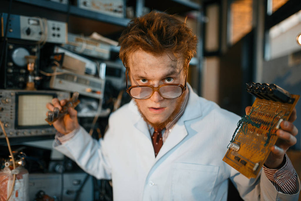 Podivný inženýr drží elektrickou trubici v laboratoři. Elektrické zkušební nástroje na pozadí. Laboratorní vybavení, inženýrská dílna - Fotografie, Obrázek