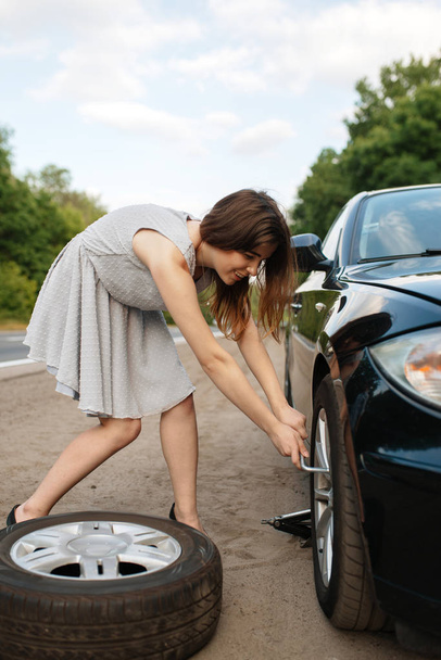 Desglose del coche, mujer joven pone el neumático de repuesto. Automóvil roto o problema con el vehículo, problemas con el neumático de automóvil perforado en la carretera
 - Foto, Imagen