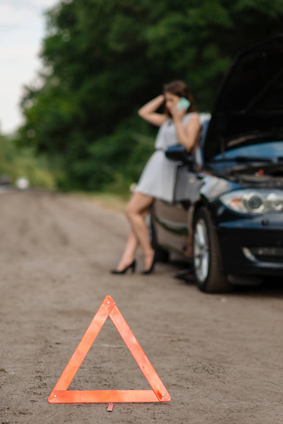 Araba arızası, acil dur işareti, yardım isteyen bir kadın. Bozuk otomobil veya araçla ilgili bir sorun, otoyolda patlamış otomobil lastiği sorunu - Fotoğraf, Görsel