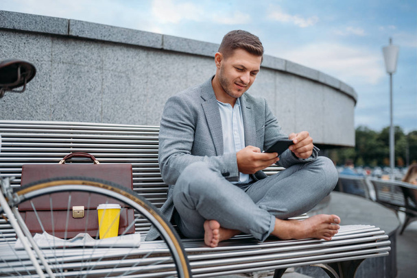 ダウンタウンのオフィスビルのベンチに自転車で休んでいるビジネスマン。街の通り、都市のスタイルでエコ輸送に乗るビジネス人 - 写真・画像